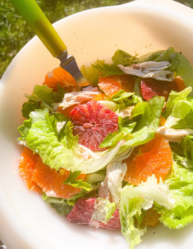 green salad with citrus fruit in white bowl with eating utensil