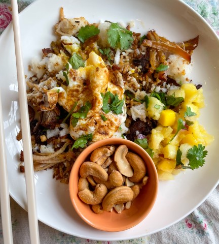 fried rice on a plate with an orange bowl of cashews and chopsticks