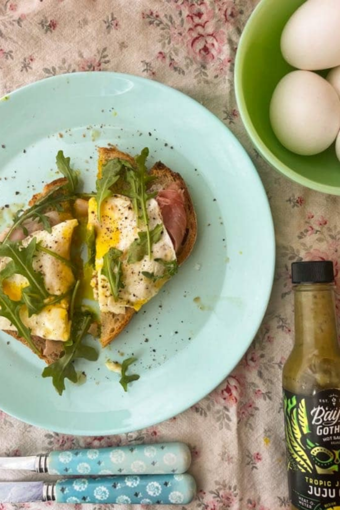 eggs on toast on a blue plate next to hot sauce and a bowl of eggs