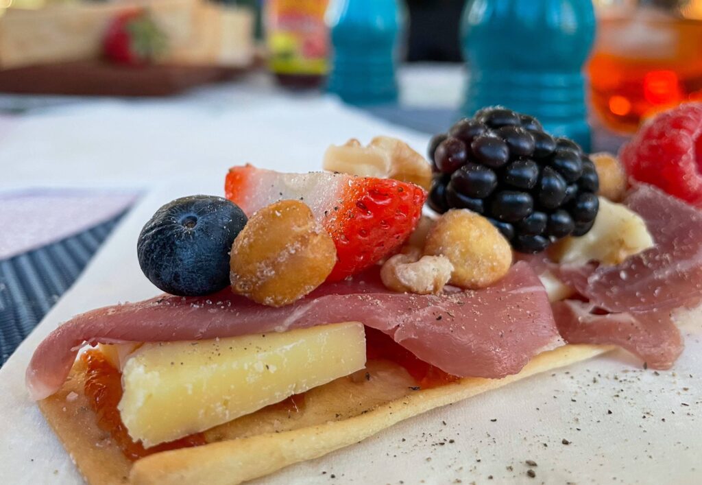 a cracker with cheese, meat, fruit, and nuts stacked on top