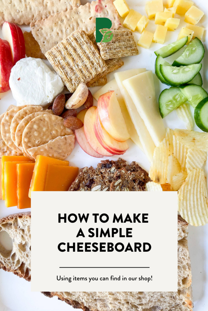 olives, apple slices, crackers, bread slices, cheese in a mug, all on a red and white checkered parchment in a light blue tray with text overlay that reads "How to make a simple cheeseboard"