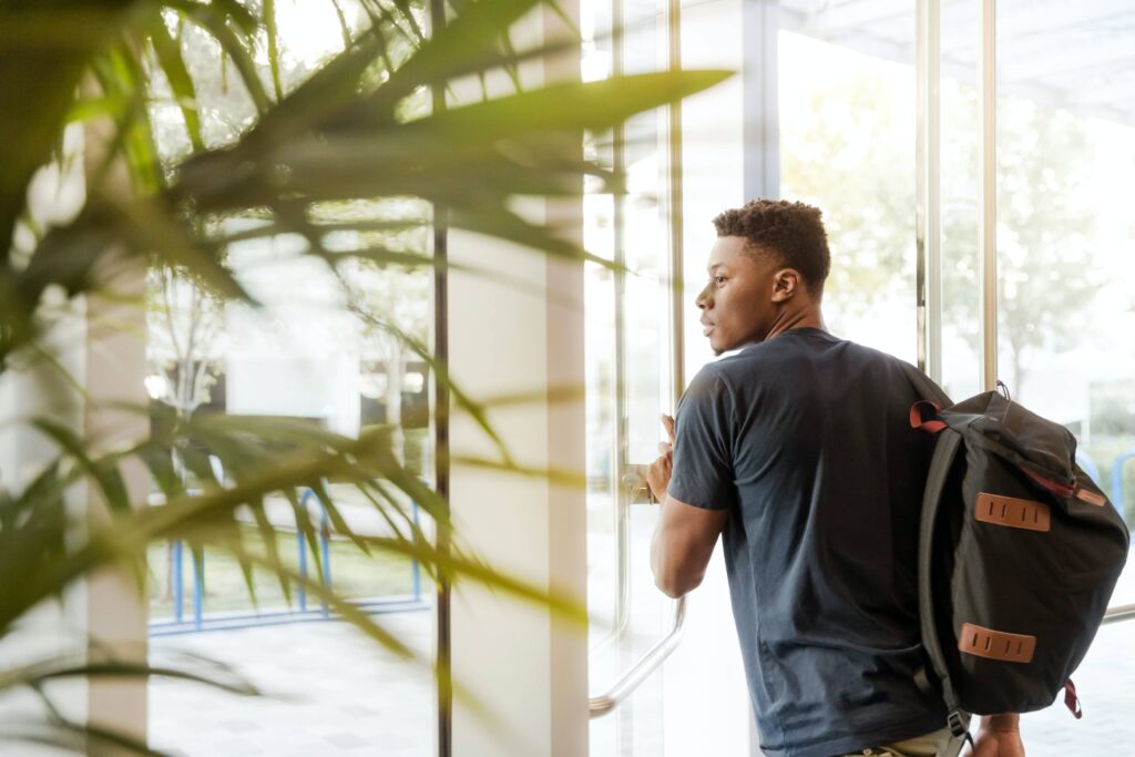 student walking through glass door by indoor plant