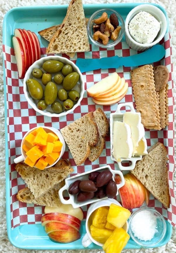 cheese, olives, sliced fruit, and breads on a red and white checkered parchment