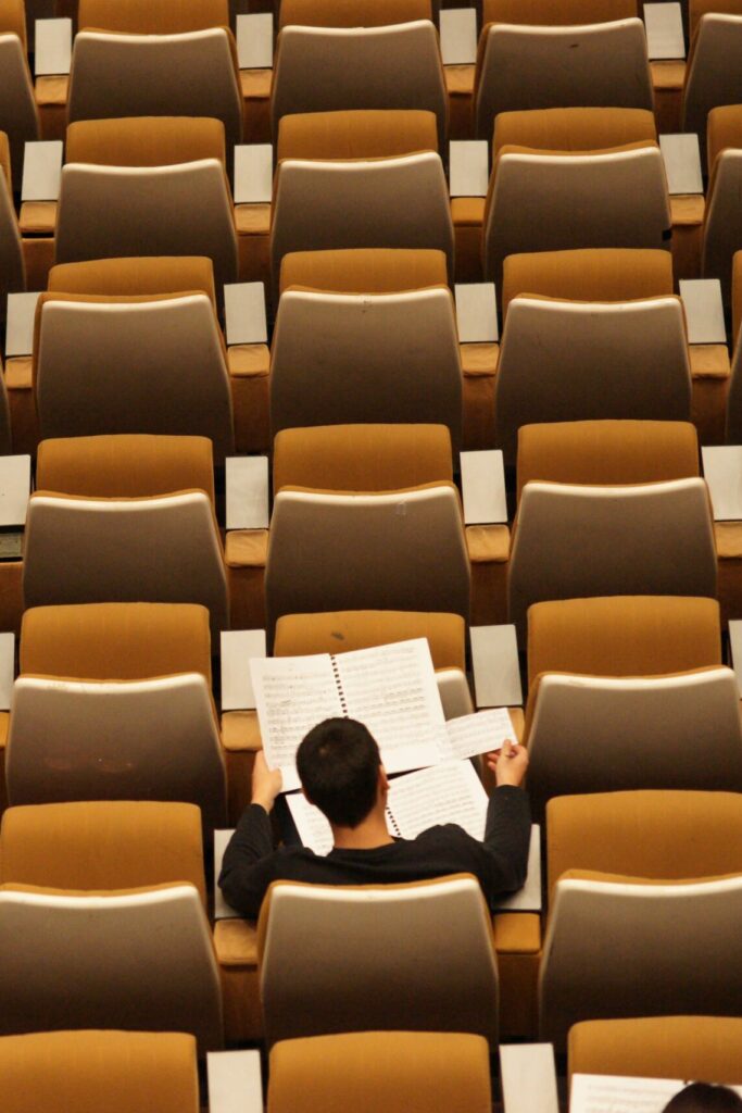 one student sitting in a theatre seat with lots of empty seats around him