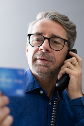 older man with glasses on phone holding credit card