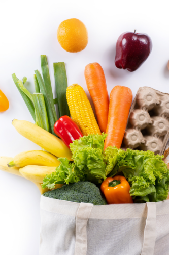 fruits, vegetables and egg carton spilling out of a white grocery sack.