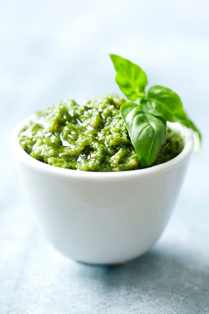 pesto in a white bowl topped with a sprig of basil