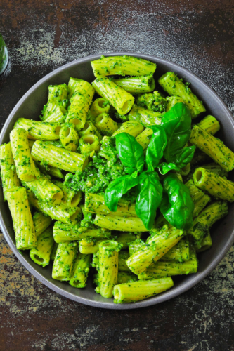 pesto pasta in a grey bowl with a sprig of basil on top