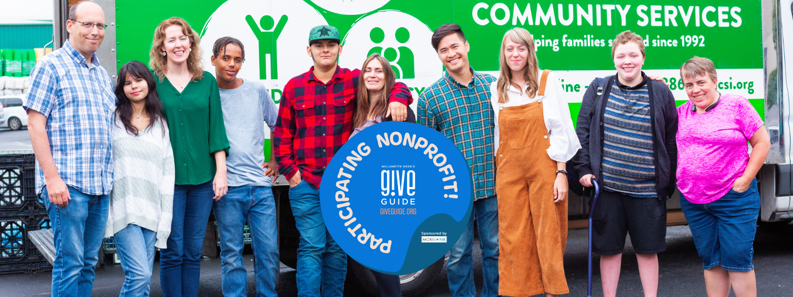 Birch participant families standing in front of the Birch box truck. From left to right: man with glasses wearing button up plaid shirt and jeans, teen girl wearing white sweater and jeans, woman in green blouse and jeans, teen boy in grey top and jeans, teen boy in plaid shirt and jeans wearing hat, woman in yoga pants and purple top with jacket, man in button up top and jeans, woman in white blouse and burnt orange jumper, teen girl in striped shirt with jacket and shorts using a cane, woman in pink top and shorts
