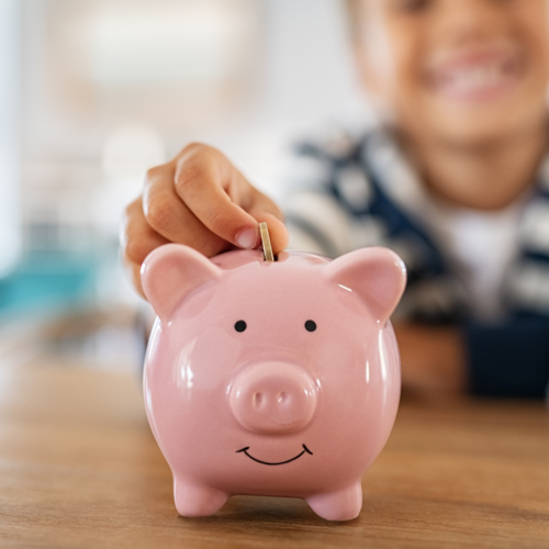 young boy placing coin into piggy bank