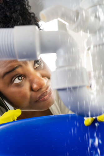 woman looking at leaky pipe under sink while on the phone